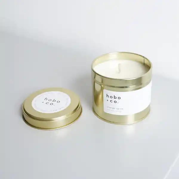 Goldene Duftkerze 'hobo + co.' mit abgenommenem Deckel auf weißem Hintergrund.