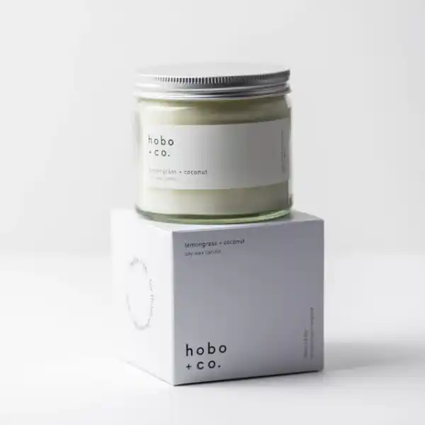 Kerze im Glas mit Zitronengras-Kokosduft von hobo + co. auf einer weißen Verpackung.