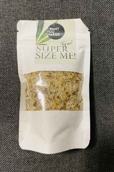 Eine Packung Badesalz mit der Aufschrift 'Super Size Me!' und 'Want You Naked' auf grauem Hintergrund.