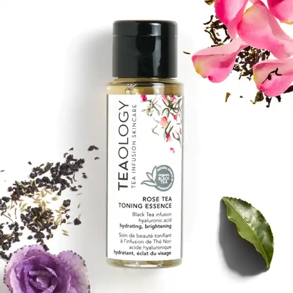 Flasche Teaology Rose Tea Toning Essence, umgeben von Teeblättern, Blütenblättern und einem grünen Blatt.
