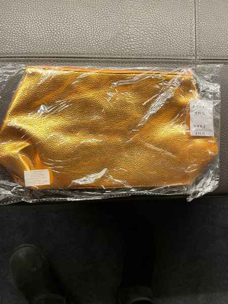 Goldene Kosmetiktasche in Plastikverpackung auf einer grauen Oberfläche.