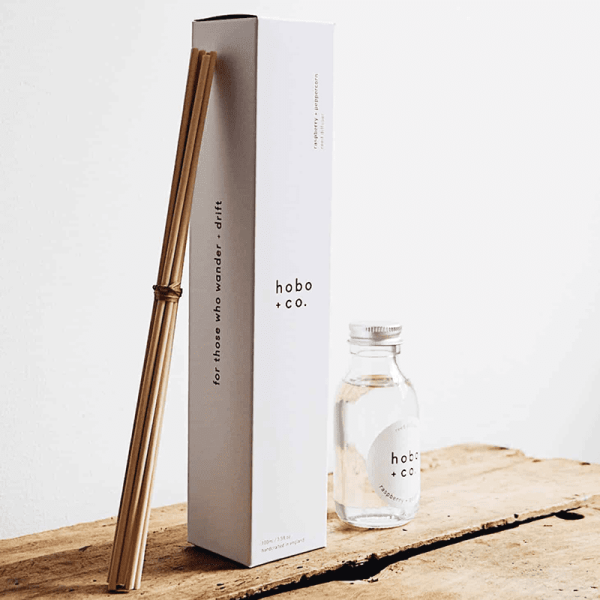 Hobo+Co. Himbeer-Pfeffer-Diffusor mit Stäbchen und Flasche auf einem Holztisch.