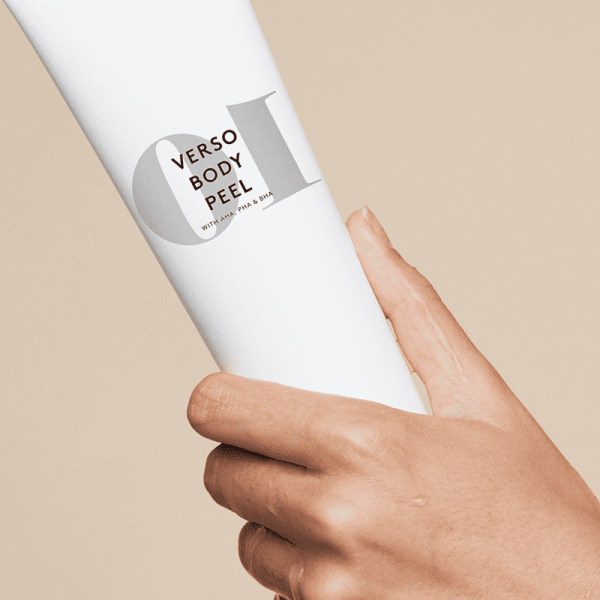 Hand hält Verso Body Peel Tube vor beigem Hintergrund.