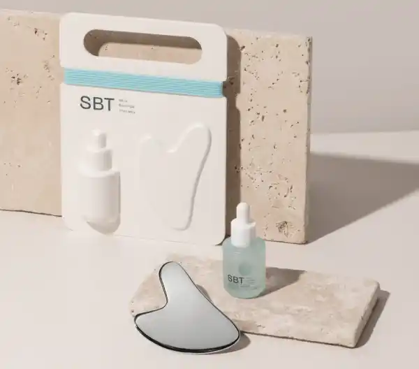 SBT Hautpflege-Set mit Serumflasche und Gua Sha Stein auf beigem Hintergrund.