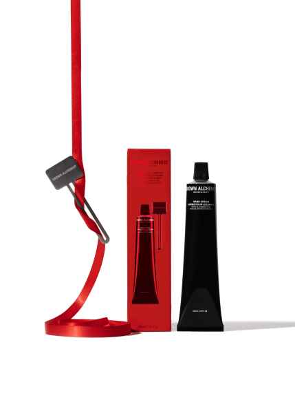 Rote Verpackung und schwarze Tube der Grown Alchemist Handcreme, daneben ein rotes Band mit Schlüssel.