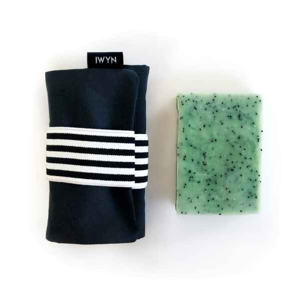 Schwarzes Handtuch mit weiß-schwarzem Band und grüne Seife mit schwarzen Punkten auf weißem Hintergrund.