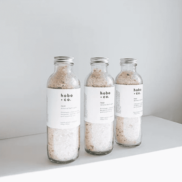 Drei Flaschen Hobo & Co. Bloom Relaxing Mineral Bath Salt auf einem weißen Regal.