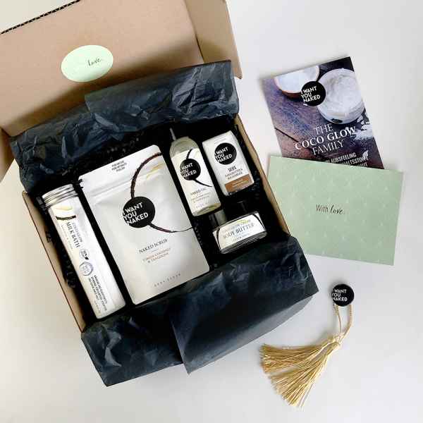 Eine geöffnete Box mit Schönheitsprodukten, darunter Peeling, Körperbutter und Broschüre, auf weißem Hintergrund.