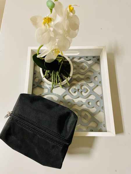 Ein weißer Blumentopf mit weißen Orchideen und eine schwarze Kosmetiktasche auf einem dekorativen Tablett.